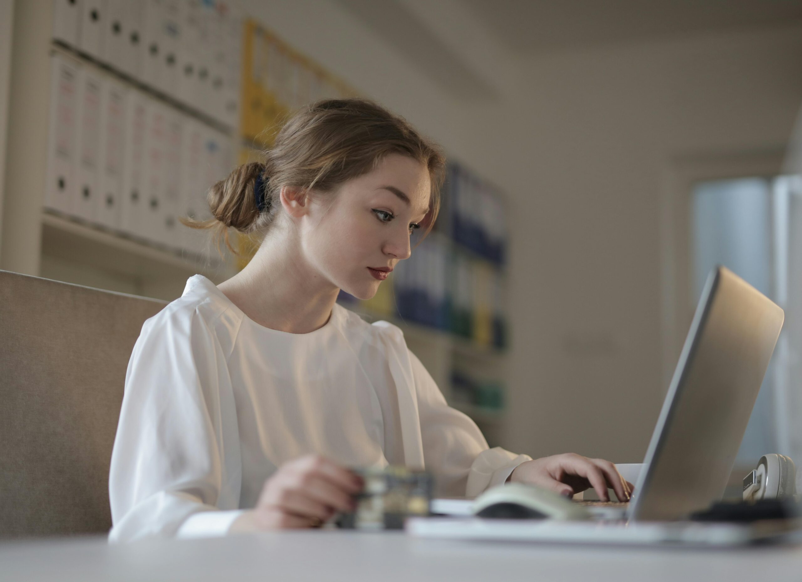 Focused woman in white working on a laptop in a modern office setting.